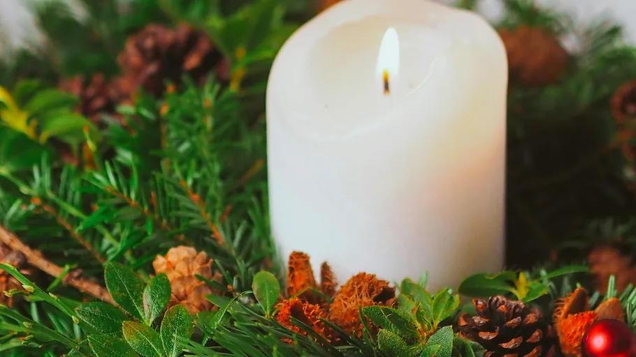White candle burning among green foliage.