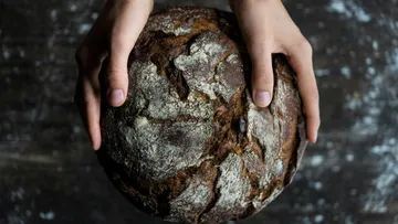 Hände halten rustikales Brotlaib auf Tisch.