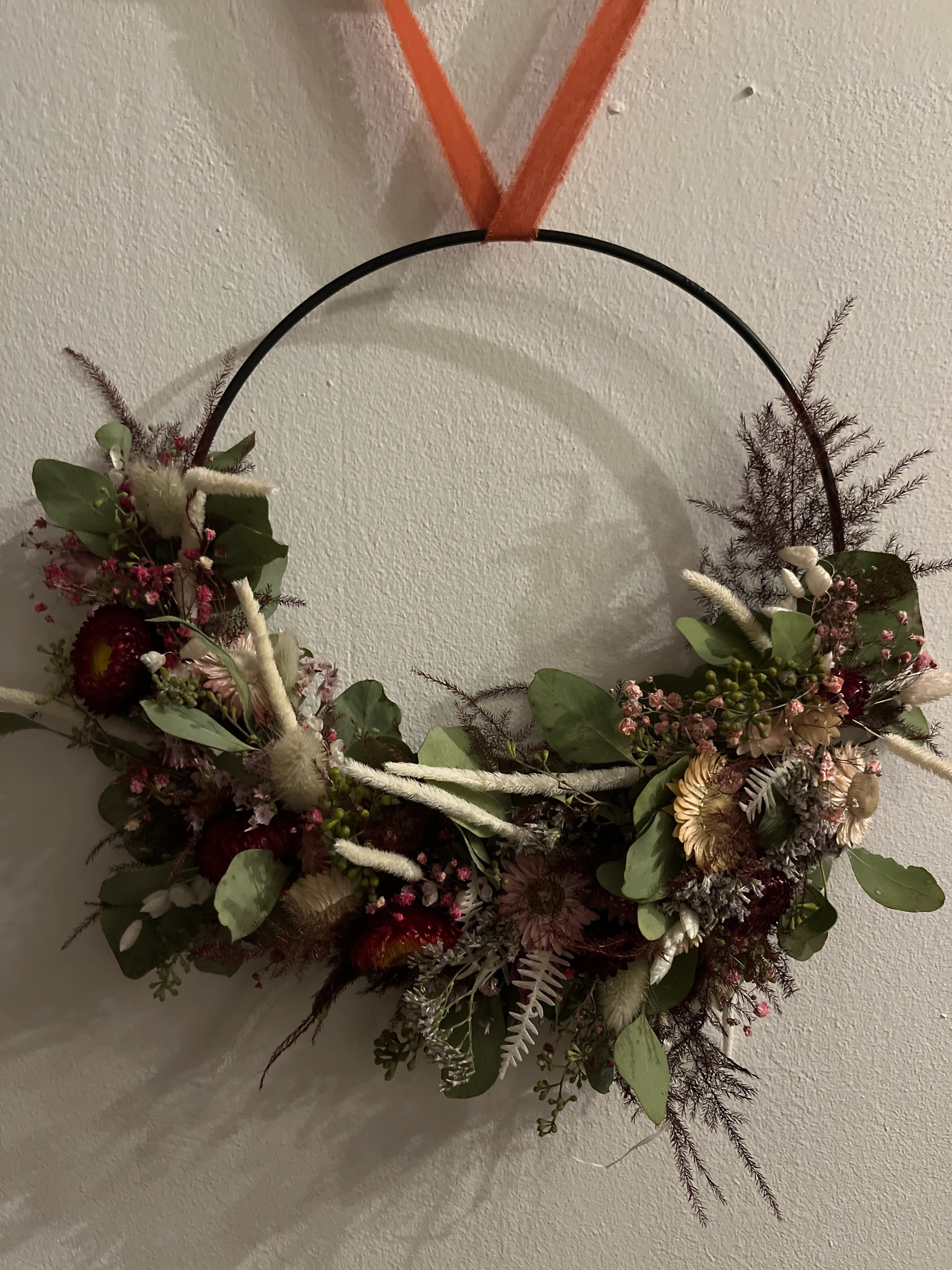 Floral wreath with greenery on white wall.