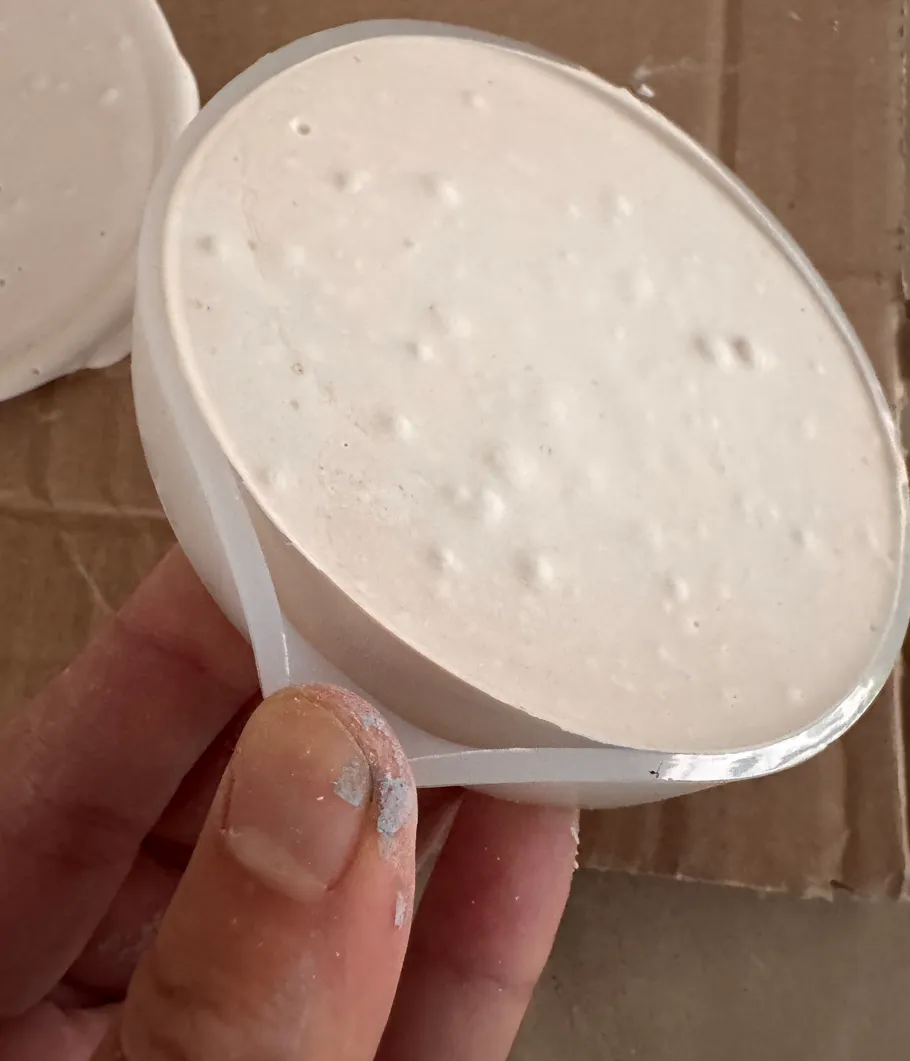 Hand holding round plaster object on cardboard.