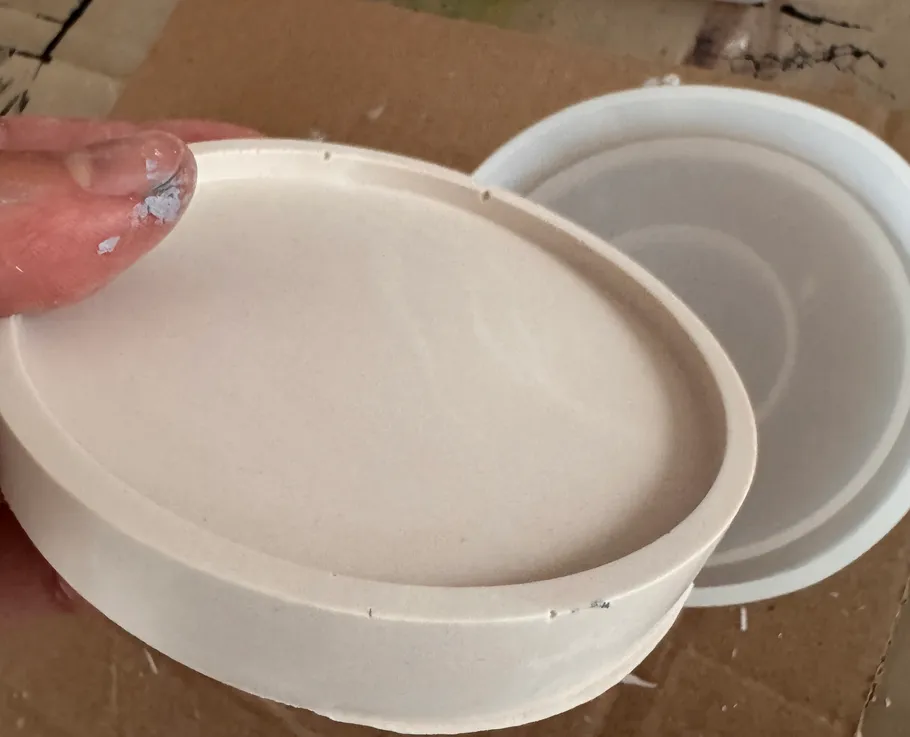 Hand holding white circular mold on cardboard.