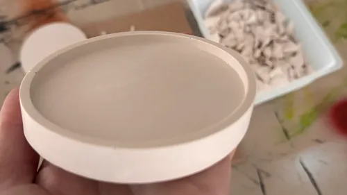 Hand holding round object above a messy table.