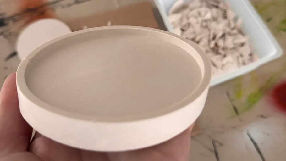 Hand holding round object above a messy table.