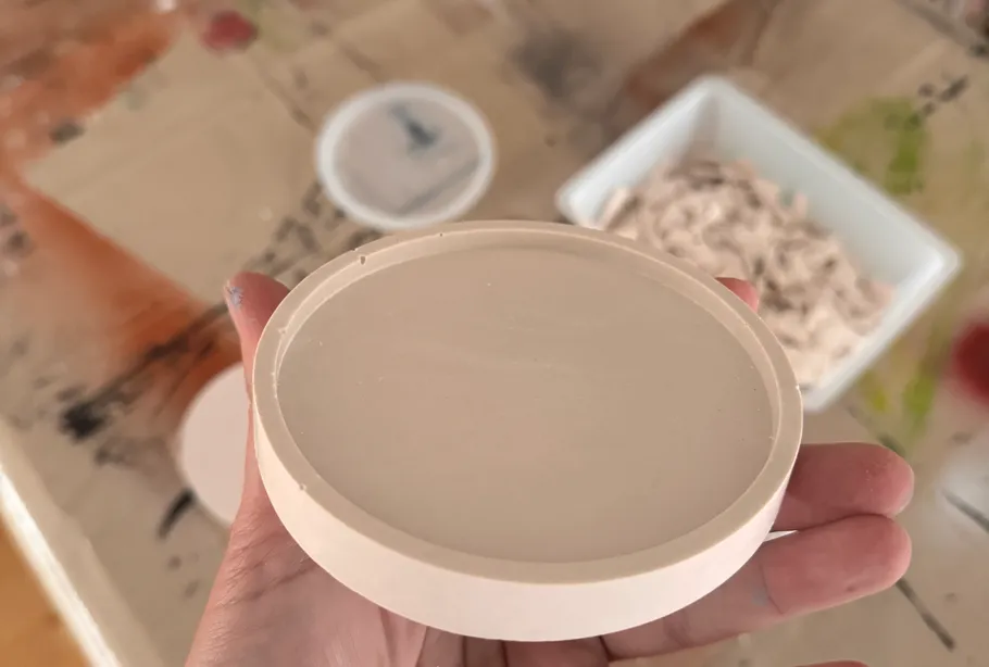 Hand holds round ceramic disc indoors.