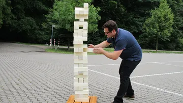 Person spielt Riesen-Jenga im Freien auf Pflaster.