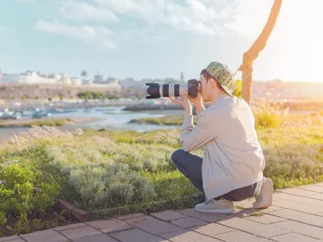 Ein Fotograf kniet und fotografiert eine Landschaft bei Sonnenlicht.