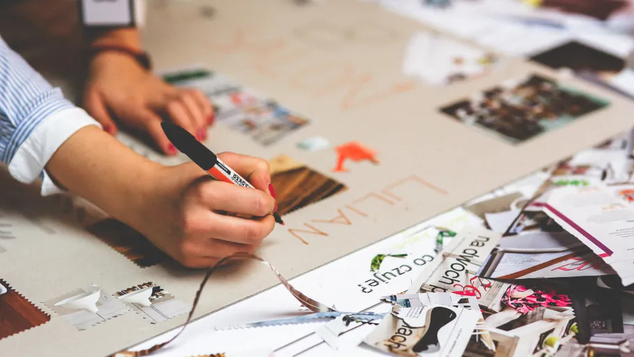 Hand schreibt auf Poster, umgeben von Papierschnipseln.
