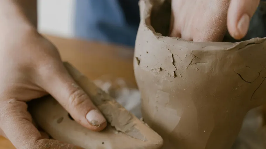 Hands shaping clay pottery on table.