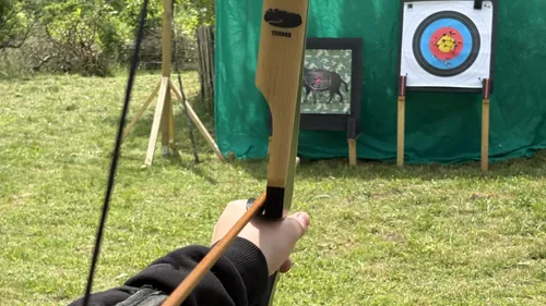 Person aiming bow at archery target outdoors.
