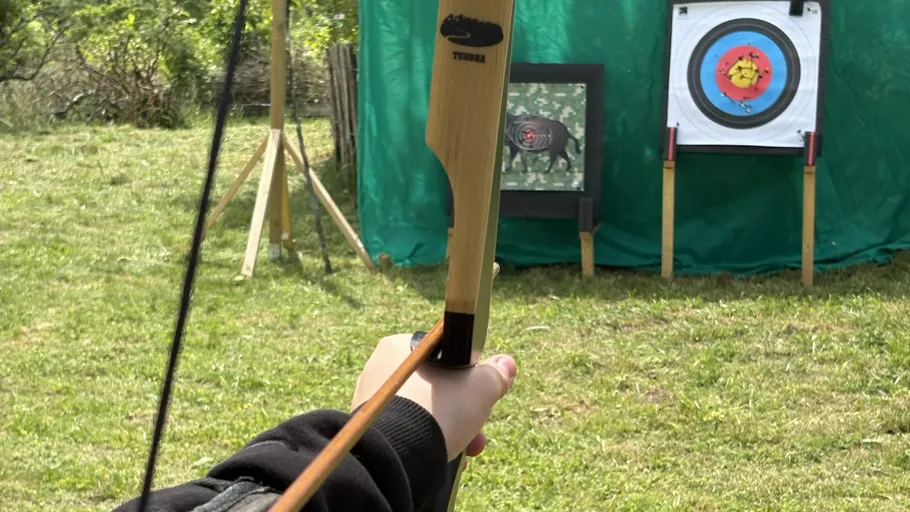 Person aiming bow at archery target outdoors.
