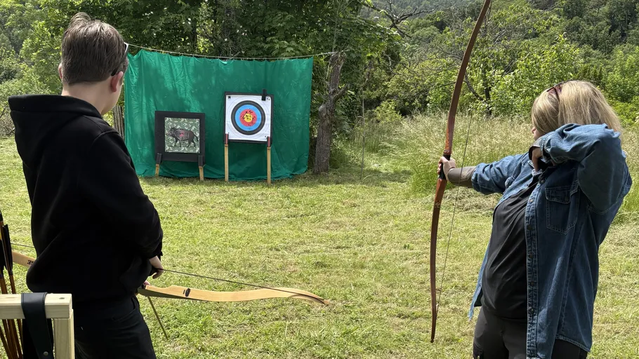 Two people practicing archery outdoors, green backdrop.