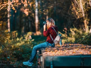Frau fotografiert sitzend auf einem Holzstamm im Wald.