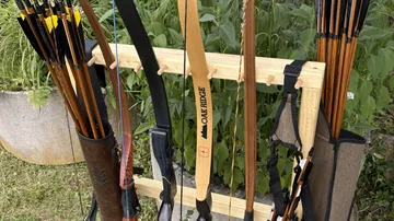Bows and arrows on wooden rack outdoors.