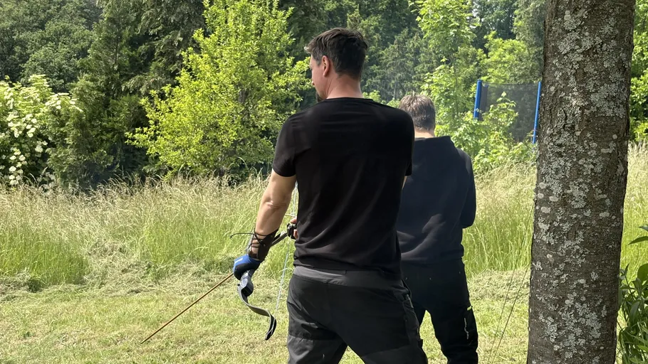 Two men practice archery in a grassy area.