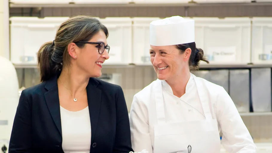 Two women smiling in a kitchen environment.