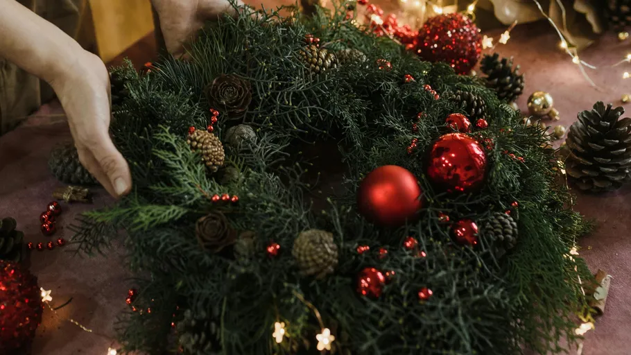 Hands arranging Christmas wreath with baubles.
