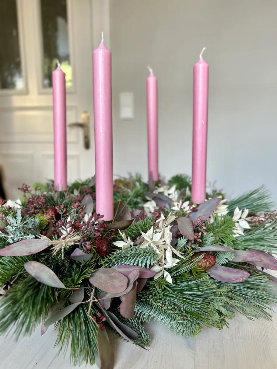Pink candles in a festive wreath on table.