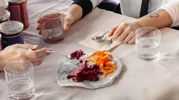 Hände essen eingelegtes Gemüse am Tisch.