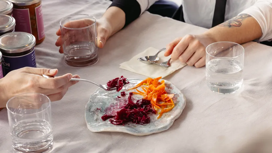 Hands eating pickled vegetables at table.