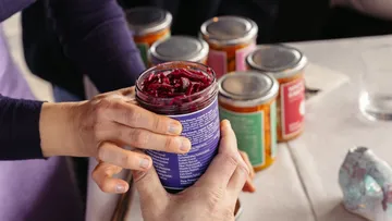Hände halten Glas mit Roter Bete auf Tisch.