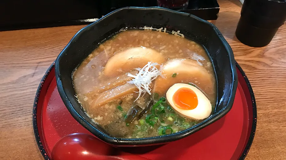 Ramen bowl with egg and pork on table.