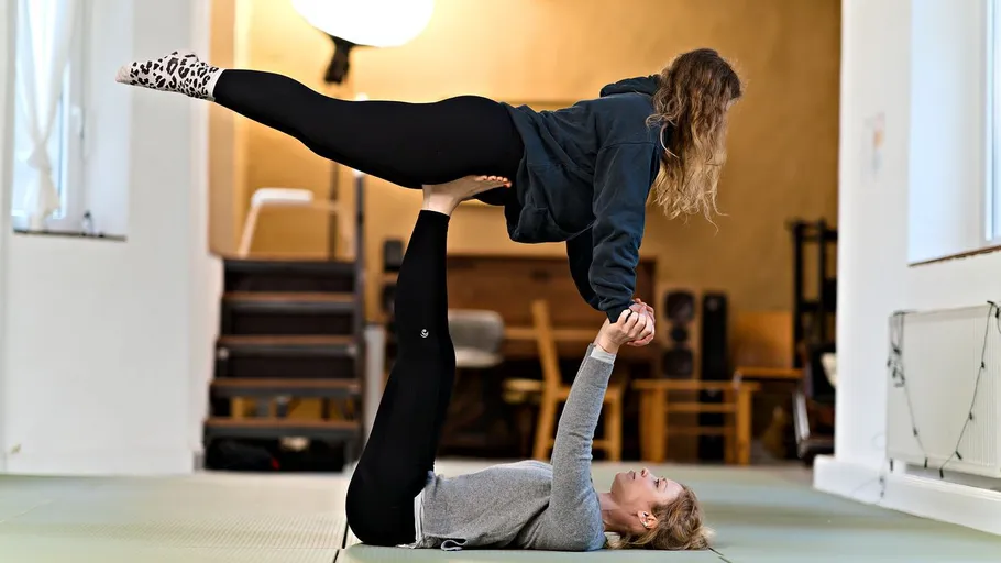 Zwei Personen üben Acro-Yoga drinnen.