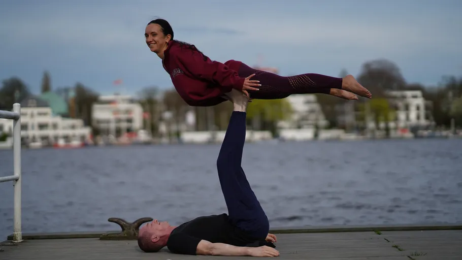 Zwei Menschen machen Akro-Yoga am Wasser.