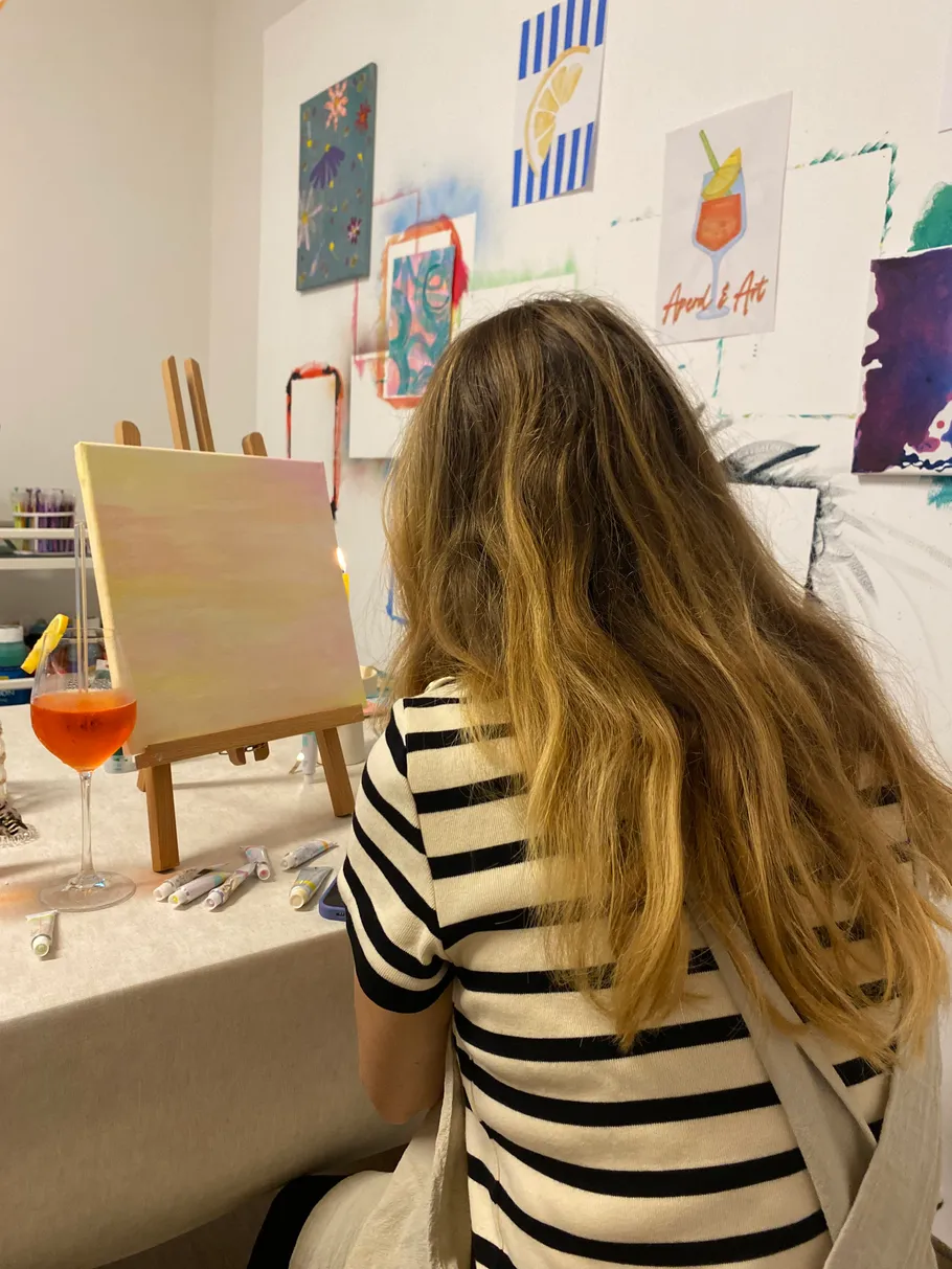Woman painting at easel with drink nearby.
