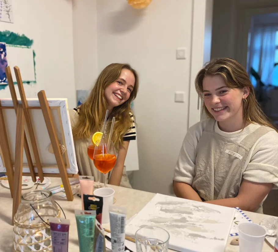 Two women painting, smiling at table.