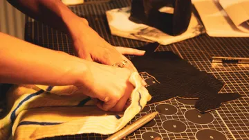 Hands crafting leather on cutting mat.
