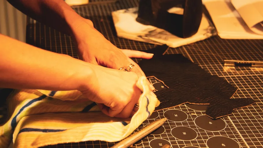 Hands crafting leather on cutting mat.