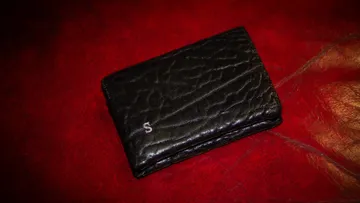 Schwarze Brieftasche auf roter, strukturierter Oberfläche.