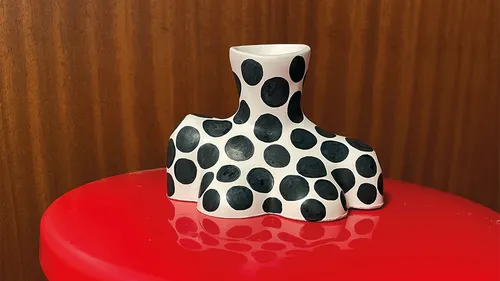 Polka dot vase on red surface, wooden background.