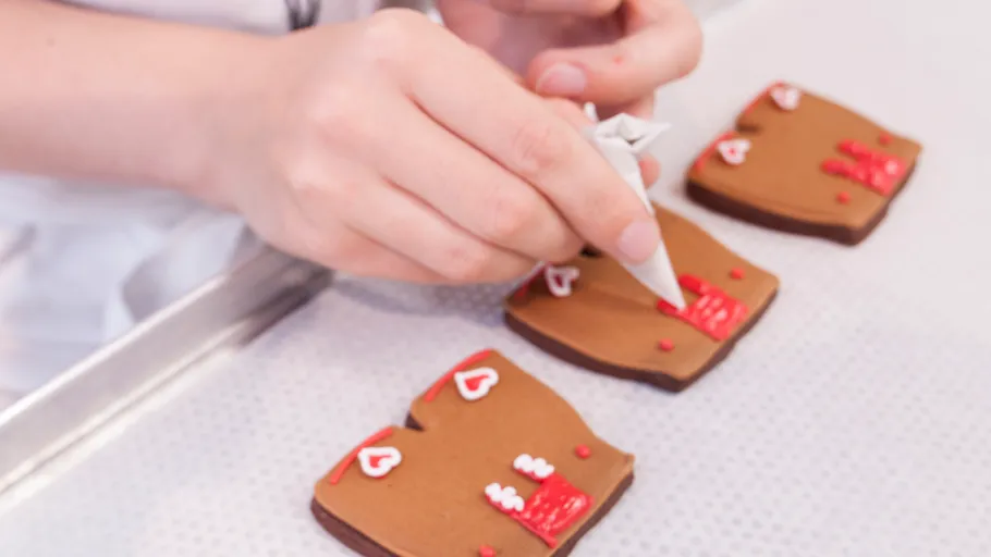 Hands decorating heart-shaped cookies on tray.