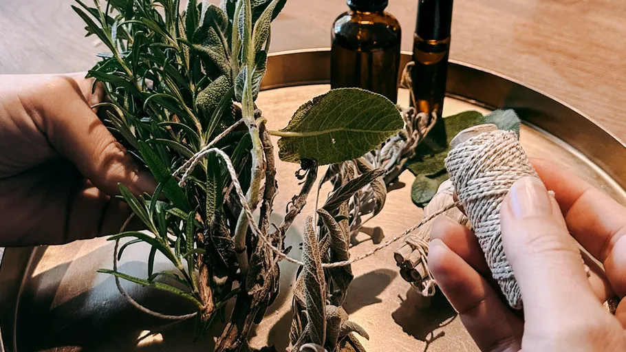 Hands tying herbs with string on tray.