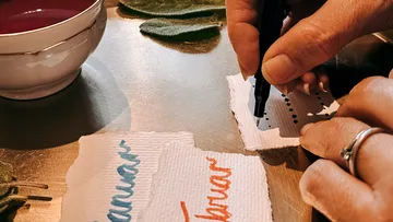 Hände schreiben auf Papier neben einer Schüssel.
