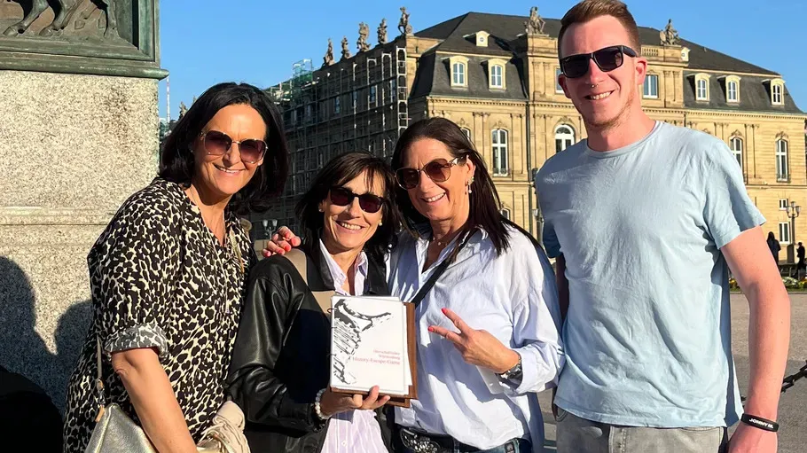 Four people posing with a plaque outside building.