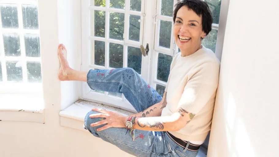 Person sitting on windowsill, smiling indoors.