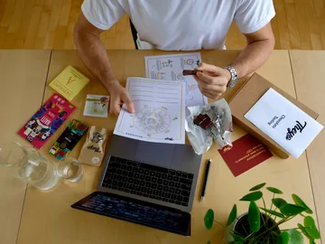 Man sits at a table, examines chocolate and writes.