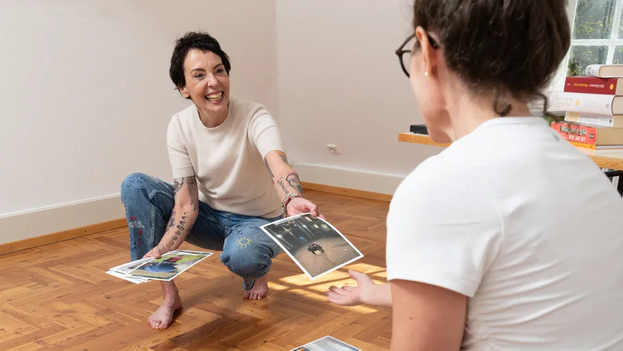 Two people exchanging photographs indoors, smiling.
