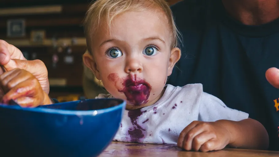 Baby with food-stained face, sitting at table.