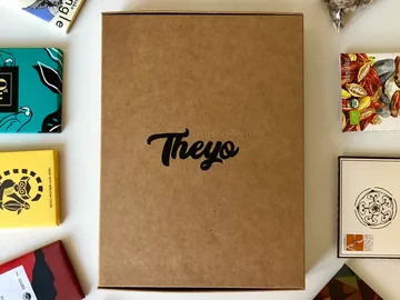Box with `Theyо` surrounded by chocolates and nuts.