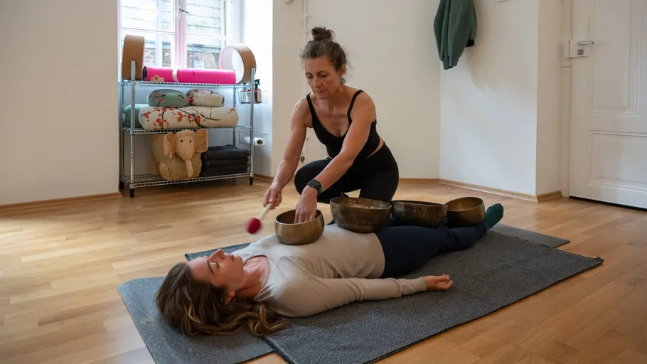 Woman holding singing bowls over another lying woman.