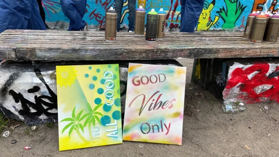 Zwei bunte Gemälde unter graffitiüberzogener Bank.