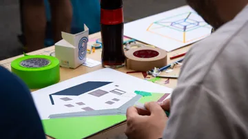Person crafting paper house at table.