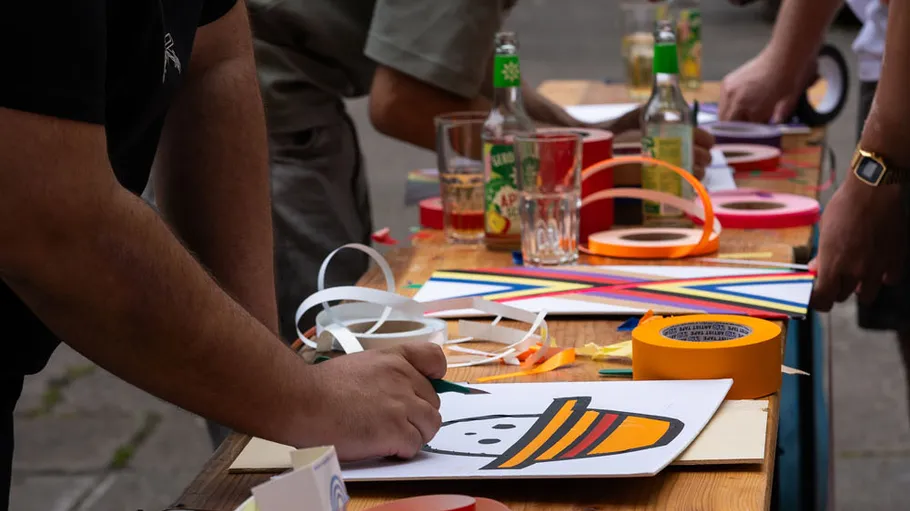 Personen basteln an Tisch im Freien mit Papier.