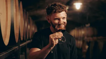 Man tasting wine in a dimly-lit cellar.