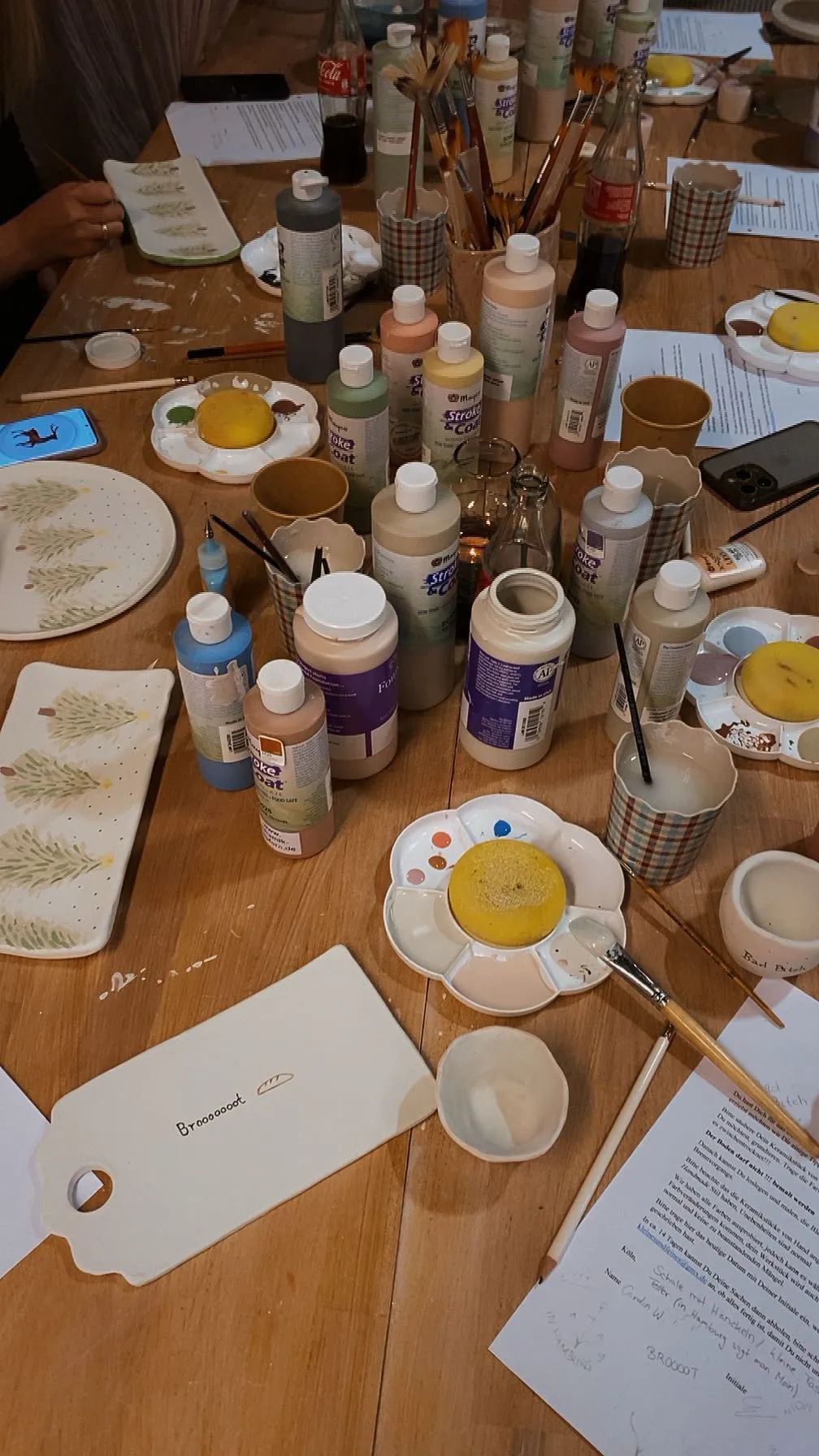 Tisch mit Farben, Pinseln und bemalter Keramik.