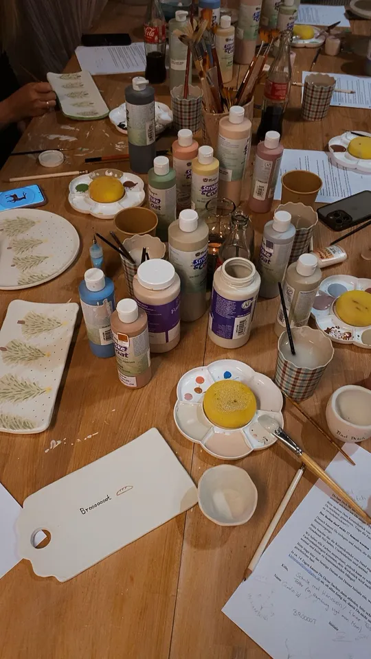 Table with paints, brushes, and painted ceramics.