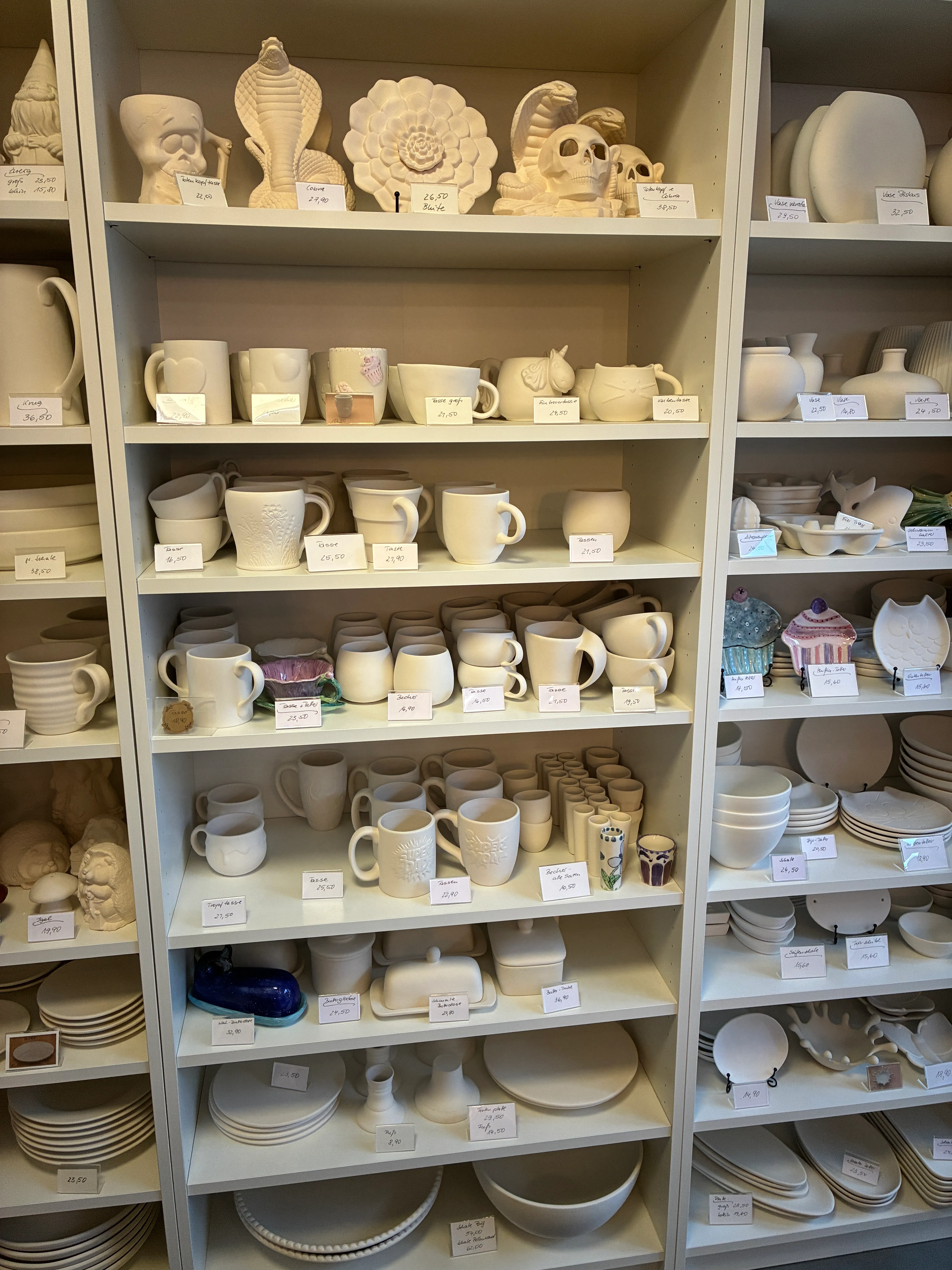 Keramikartikel auf Regalen mit Preisschildern ausgestellt.